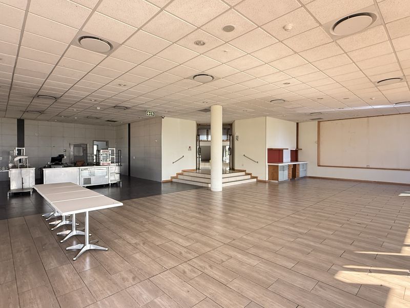 Spacious open-plan industrial area featuring a suspended ceiling, recessed lighting, and durable tiled flooring, suitable for a variety of commercial or office uses.