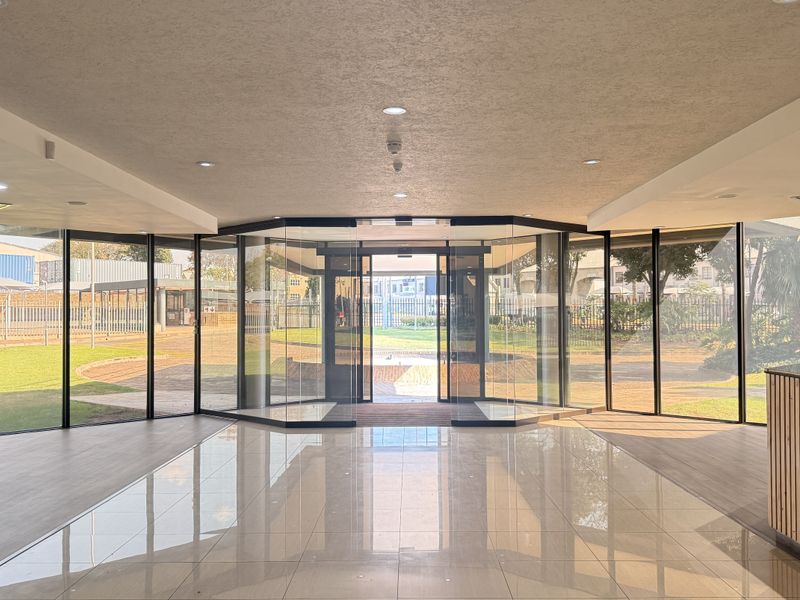 Modern, bright entrance lobby featuring floor-to-ceiling glass walls, polished tiled flooring, and a built-in reception desk with a clean, professional aesthetic.