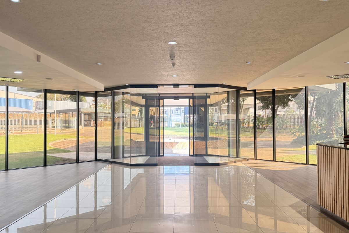 Modern, bright entrance lobby featuring floor-to-ceiling glass walls, polished tiled flooring, and a built-in reception desk with a clean, professional aesthetic.