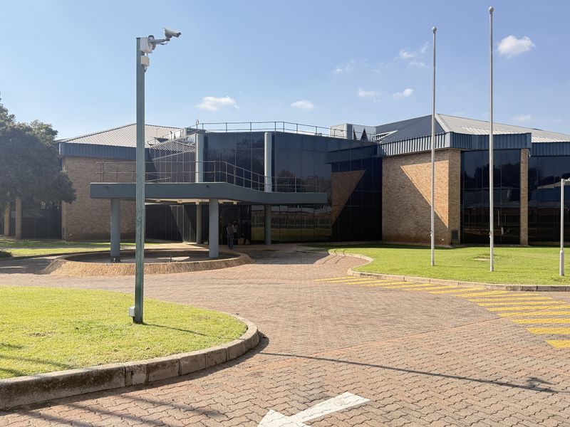 Front exterior view of a professional industrial building featuring a brick facade, tinted glass curtain walls, and a paved driveway with a covered entrance.