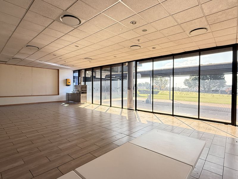 Spacious open-plan industrial unit featuring large floor-to-ceiling windows, tiled flooring, and a suspended ceiling with recessed lighting.