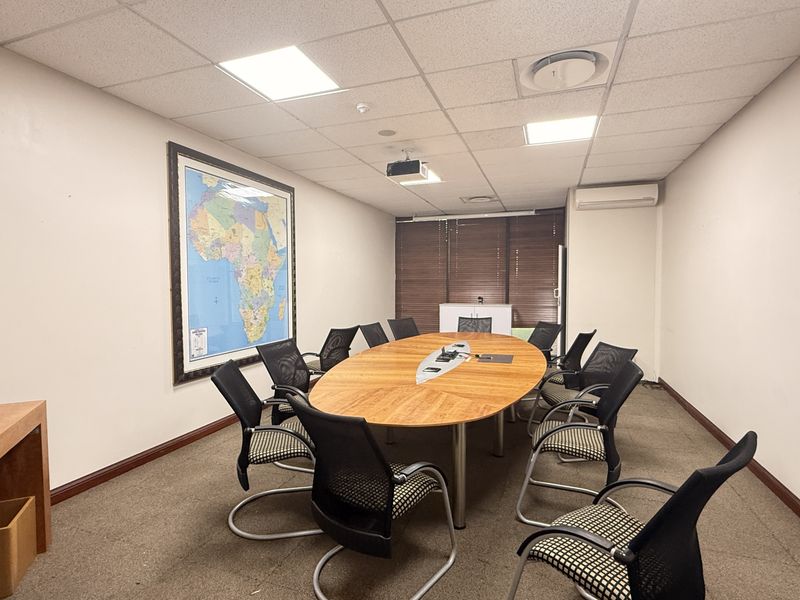 A functional office meeting room featuring a suspended ceiling, recessed lighting, air conditioning, and carpeted flooring, suitable for professional use.