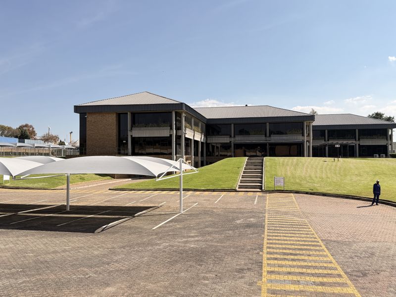 Exterior view of a multi-story industrial office building featuring a paved parking area with shade cloth carports and landscaped grounds.