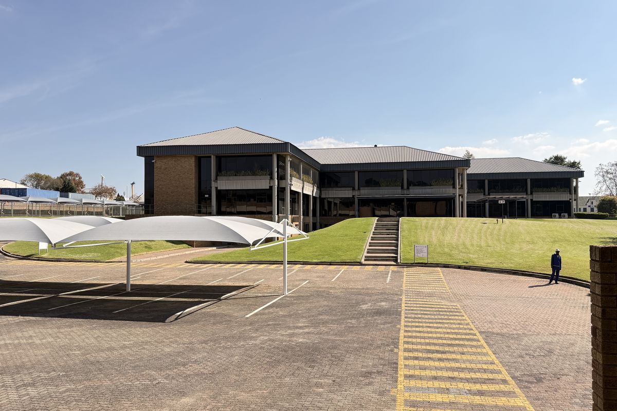 Exterior view of a multi-story industrial office building featuring a paved parking area with shade cloth carports and landscaped grounds.