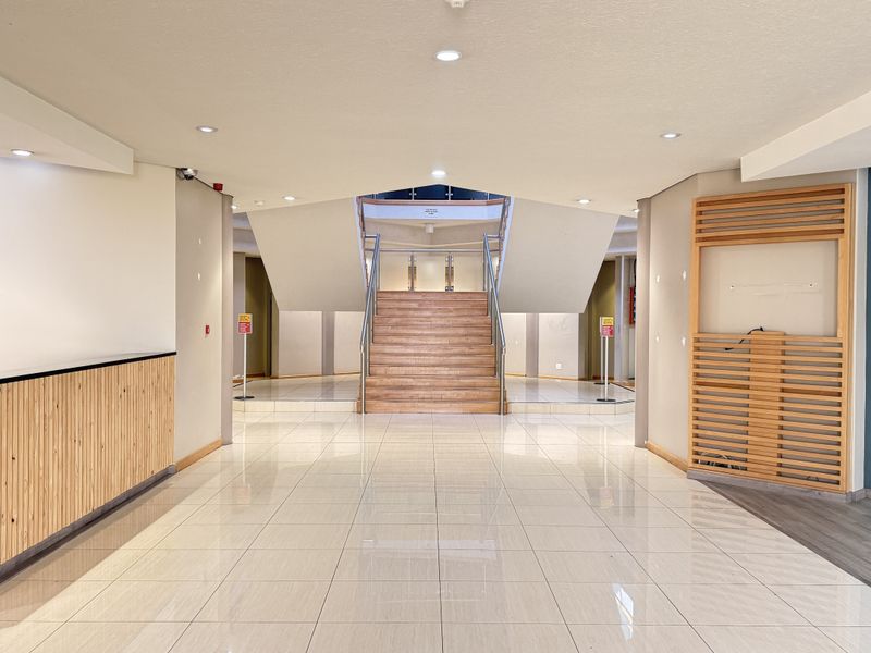 Spacious industrial entrance lobby featuring a modern reception desk, tiled flooring, and a central staircase with wooden treads and metal handrails.