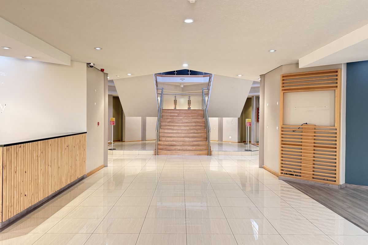Spacious industrial entrance lobby featuring a modern reception desk, tiled flooring, and a central staircase with wooden treads and metal handrails.