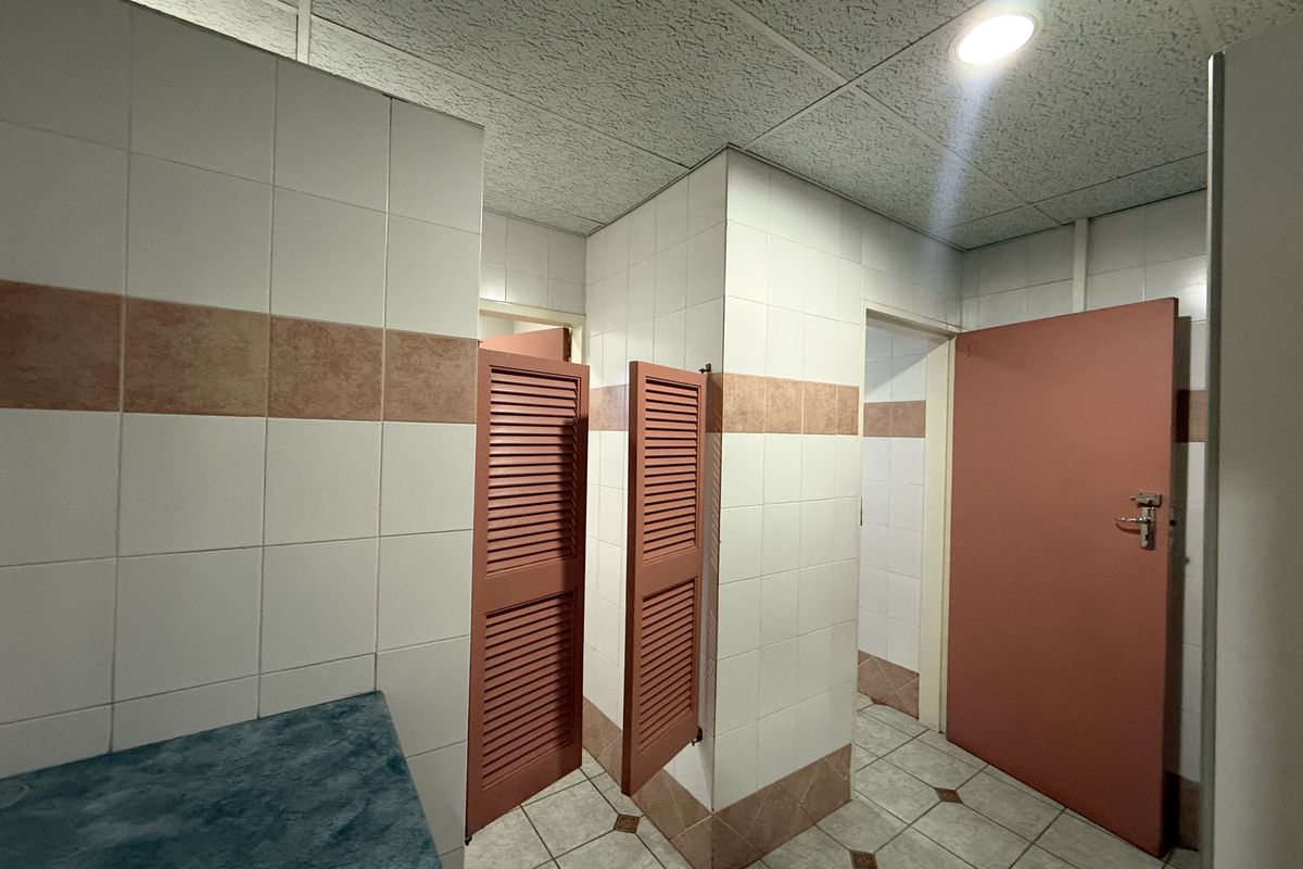 A functional commercial bathroom space featuring tiled walls, louvered doors, and a suspended ceiling, currently in a dated condition.