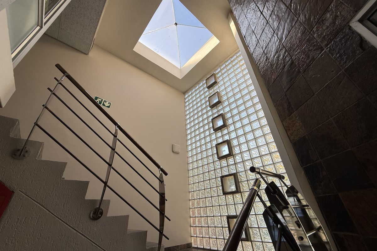 A bright commercial hallway featuring a large skylight, a decorative glass block wall, and a modern staircase with metal handrails.