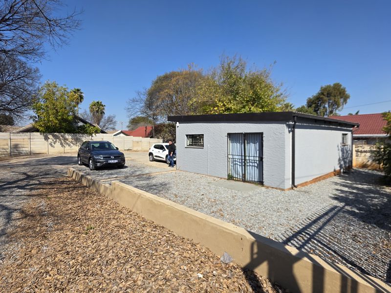 A detached office building featuring a gravel parking area, secure entrance gate, and perimeter walling in a well-maintained outdoor space.
