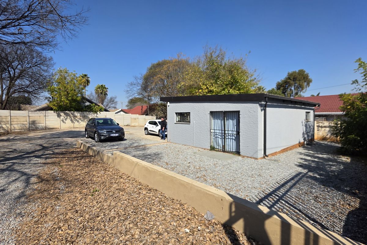 A detached office building featuring a gravel parking area, secure entrance gate, and perimeter walling in a well-maintained outdoor space.