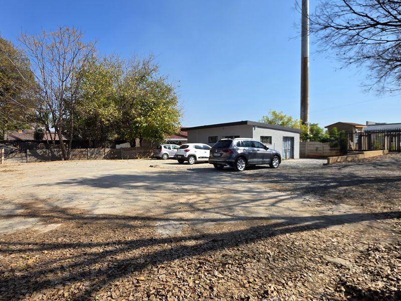 An exterior view of the office property featuring a large open parking area, perimeter fencing, and a single-story office building structure.