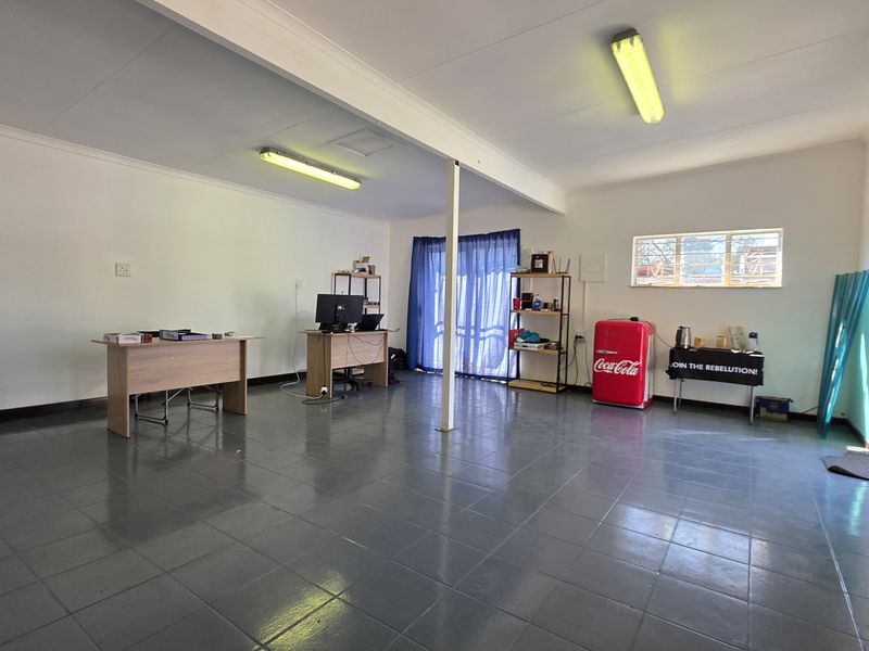Spacious open-plan office area featuring tiled flooring, fluorescent lighting, and direct access to the exterior via a sliding glass door.