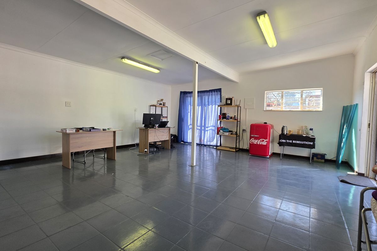 Spacious open-plan office area featuring tiled flooring, fluorescent lighting, and direct access to the exterior via a sliding glass door.