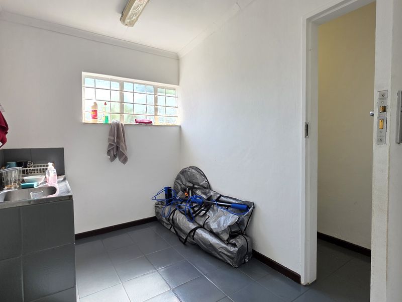 A functional laundry room featuring tiled flooring, a stainless steel sink with a tiled splashback, and a window for natural light.