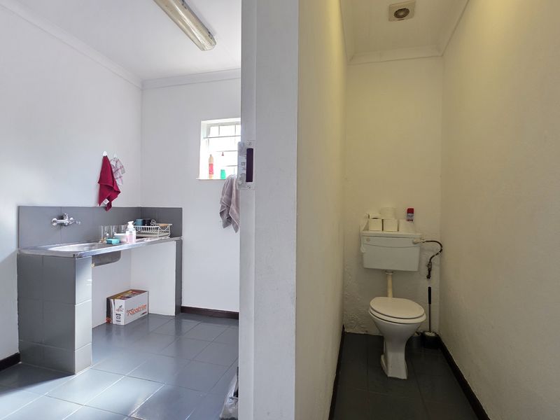 A functional utility space featuring a stainless steel sink area and a separate enclosed toilet with basic fixtures.