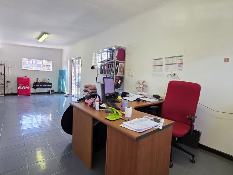 A functional office space featuring tiled flooring, fluorescent lighting, and large windows, providing a practical work environment with potential for modernization.