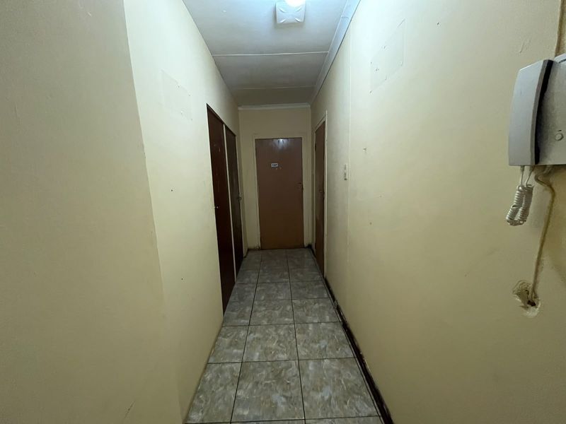 A functional interior hallway featuring tiled flooring, multiple access doors, and a wall-mounted intercom system, requiring cosmetic updates to the walls and finishes.