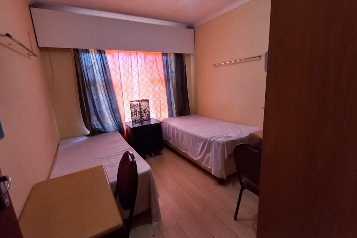 A compact bedroom featuring laminate flooring and a built-in curtain pelmet, currently configured with twin beds.