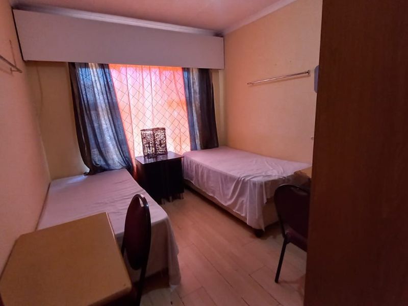 A compact bedroom featuring laminate flooring and a built-in curtain pelmet, currently configured with twin beds.