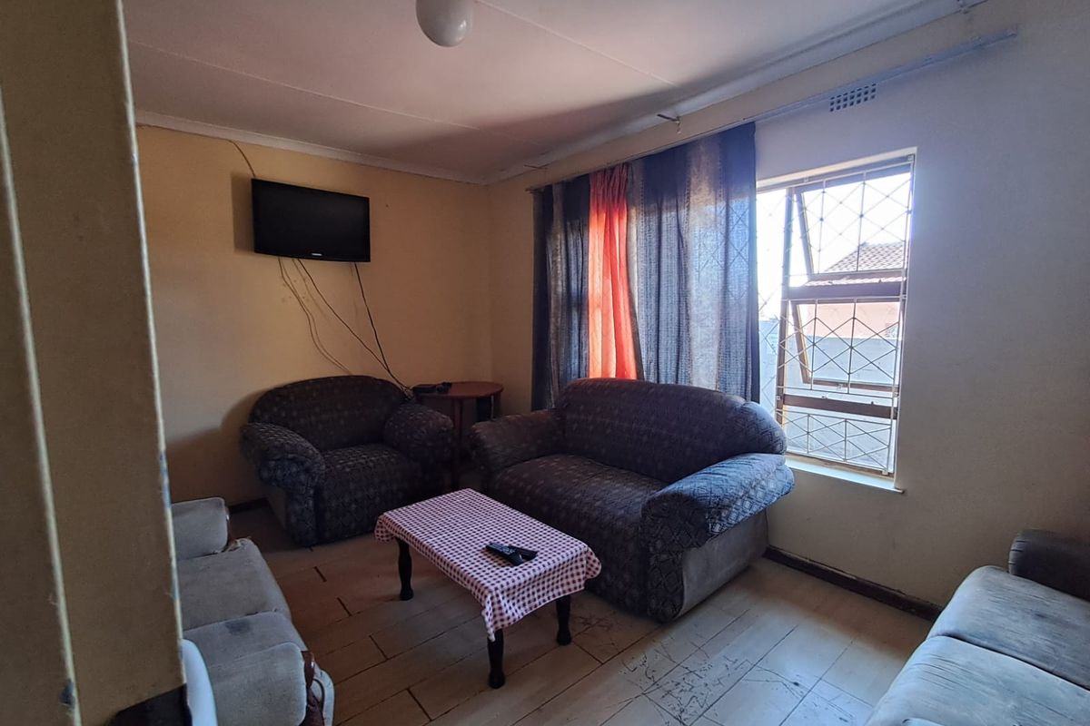A living room area featuring tiled flooring, security window bars, and wall-mounted television space, requiring cosmetic updates to improve the overall aesthetic.