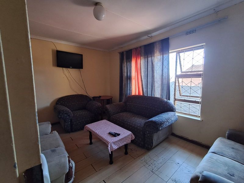 A living room area featuring tiled flooring, security window bars, and wall-mounted television space, requiring cosmetic updates to improve the overall aesthetic.