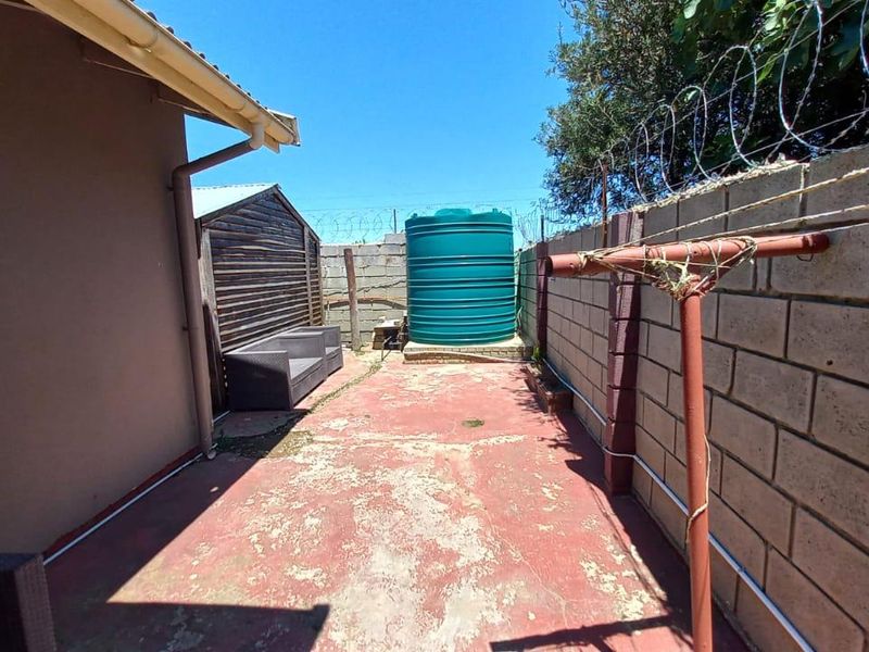 Rear exterior area featuring a water storage tank, concrete block boundary wall with security fencing, and paved ground surface.