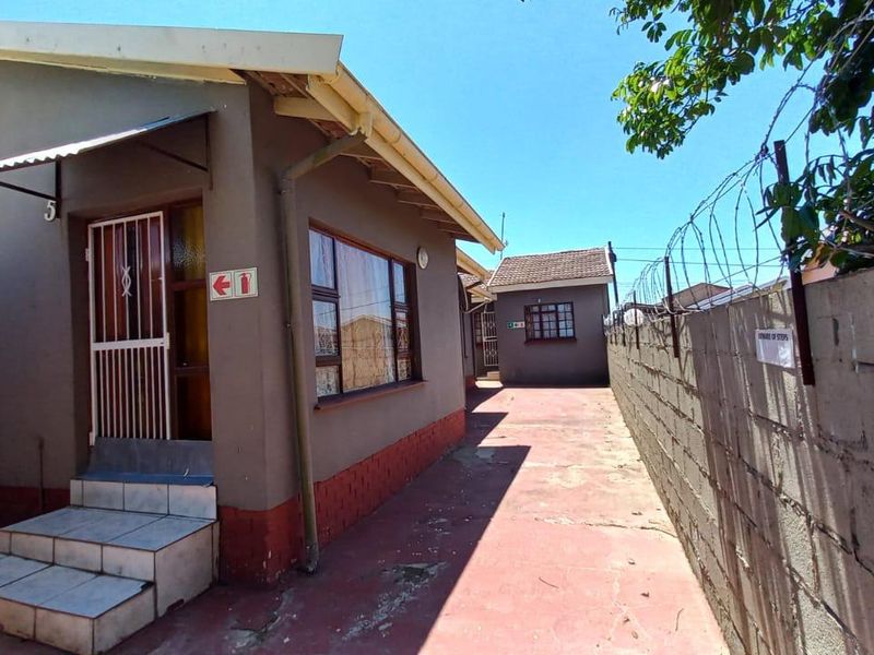 Exterior view of a commercial property featuring a paved side walkway, security fencing, and tiled entrance steps leading to the building.