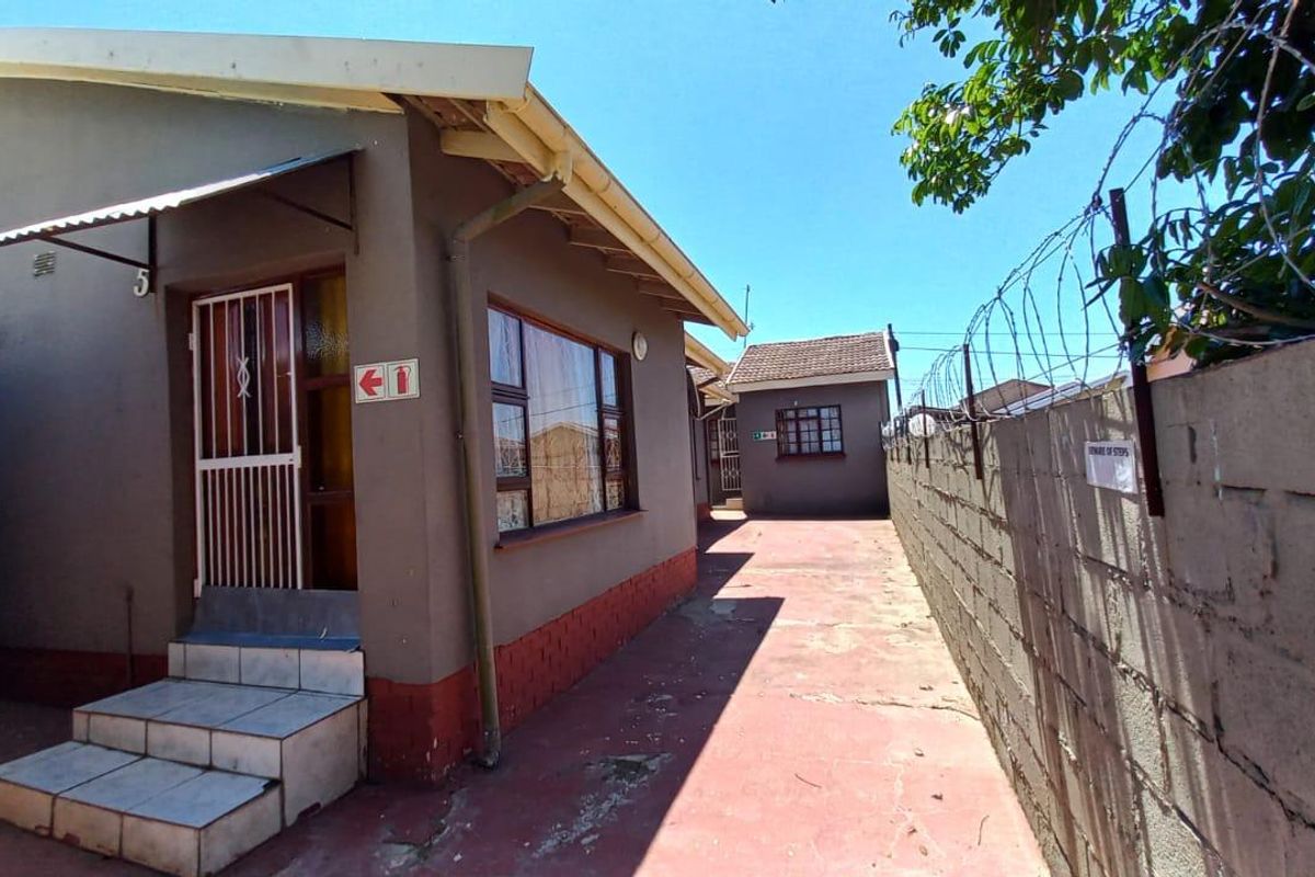 Exterior view of a commercial property featuring a paved side walkway, security fencing, and tiled entrance steps leading to the building.