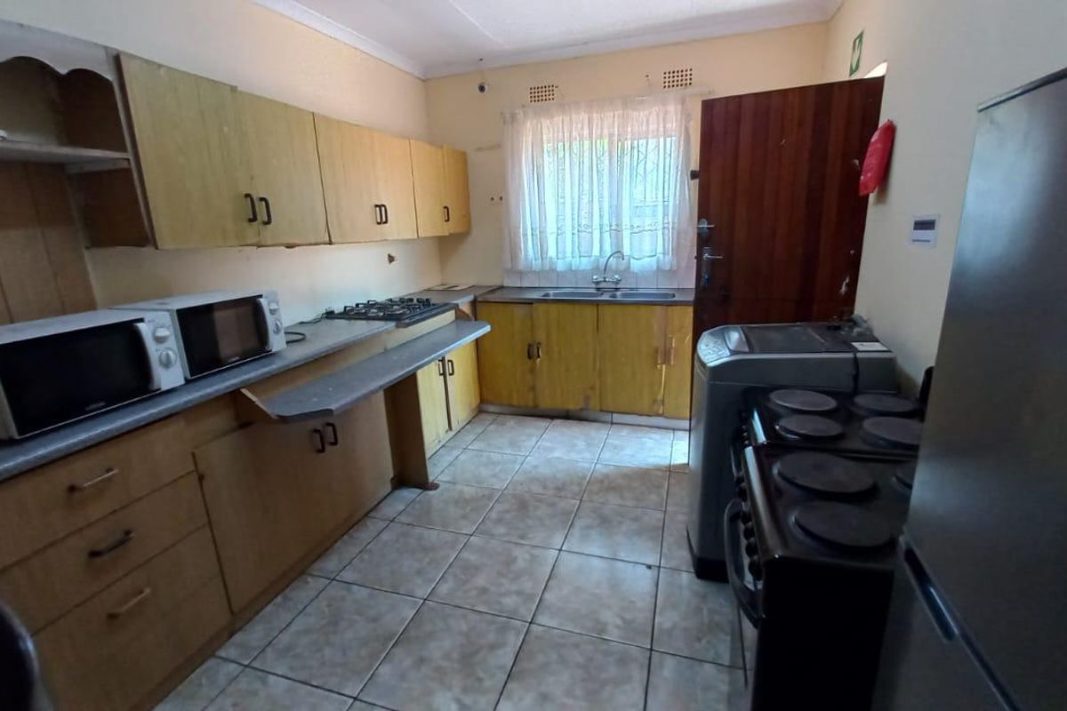 Functional kitchen featuring wooden cabinetry, tiled flooring, and a gas hob, offering a practical layout with potential for cosmetic modernization.