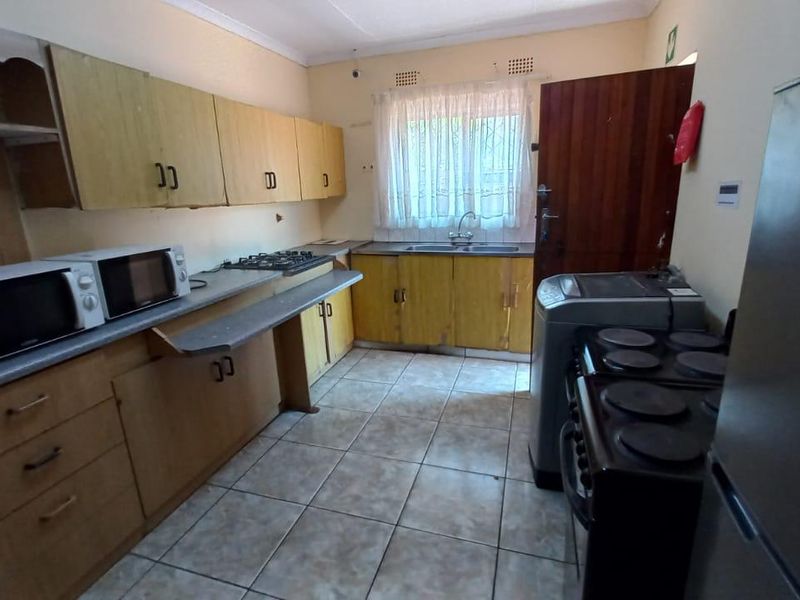 Functional kitchen featuring wooden cabinetry, tiled flooring, and a gas hob, offering a practical layout with potential for cosmetic modernization.