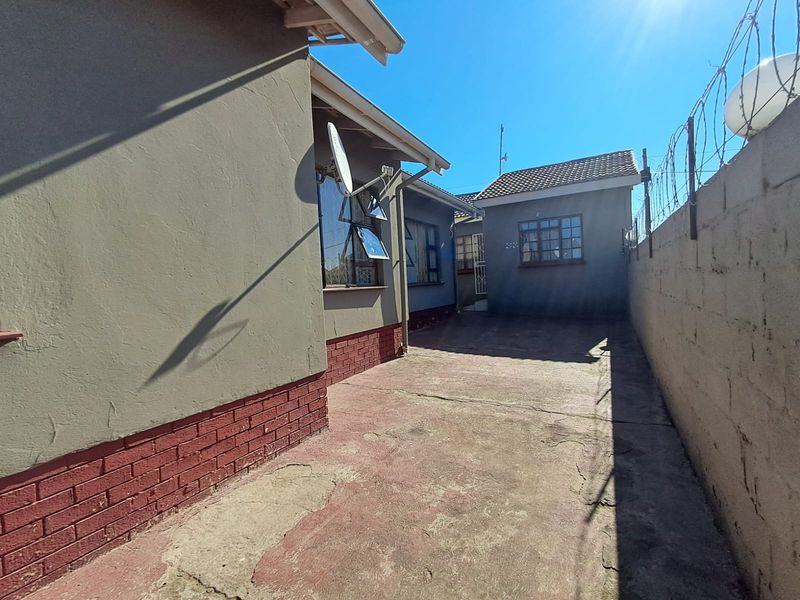 Rear exterior view showing a paved courtyard area, perimeter wall with security fencing, and building facade with security bars on windows.