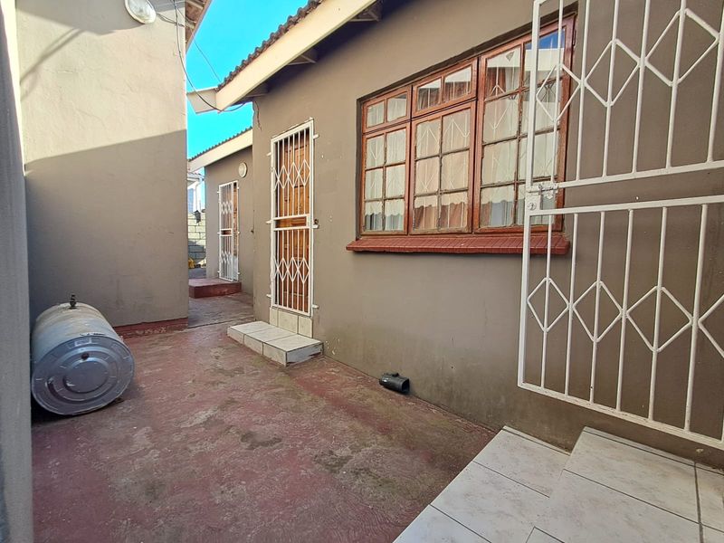 Rear exterior view showing a paved courtyard area with security gates and timber-framed windows on the building facade.