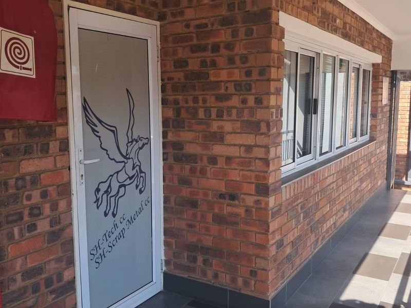 Exterior view of an office entrance featuring face brick walls, an aluminium framed glass door, and a fire hose reel installation.
