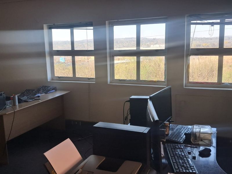 A functional office space featuring large windows with natural light, carpeted flooring, and built-in storage, suitable for a professional workspace.