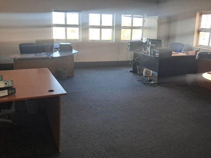 A functional office space featuring carpeted flooring and multiple windows providing natural light, suitable for a professional work environment.