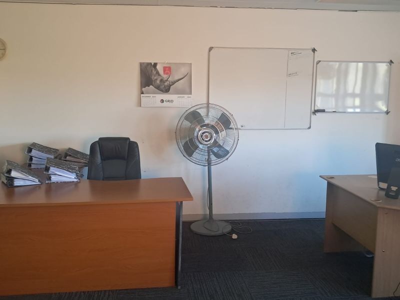 A functional office space featuring carpeted flooring, built-in storage cabinets, and wall-mounted whiteboards, suitable for a professional work environment.