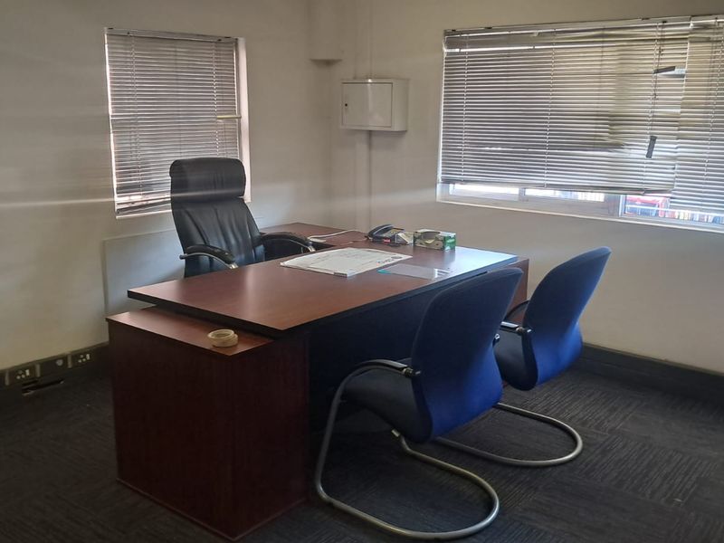 A functional office space featuring carpeted flooring, large windows with venetian blinds, and wall-mounted electrical infrastructure.