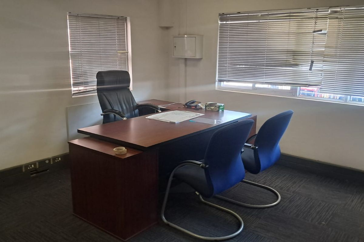 A functional office space featuring carpeted flooring, large windows with venetian blinds, and wall-mounted electrical infrastructure.