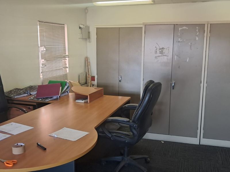 A functional office space featuring built-in storage cupboards, carpeted flooring, and natural light through a window with venetian blinds.