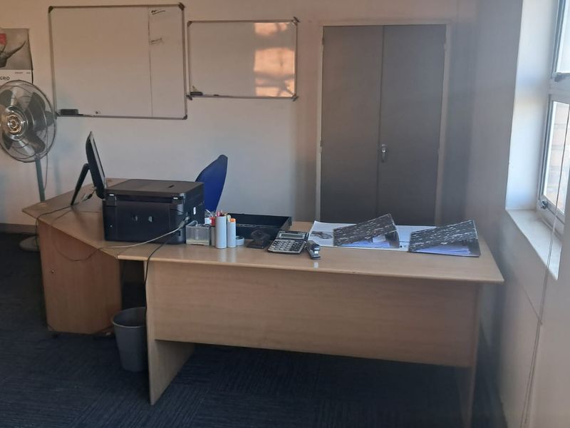 A functional office space featuring carpeted flooring, a built-in storage cupboard, and large windows providing natural light.