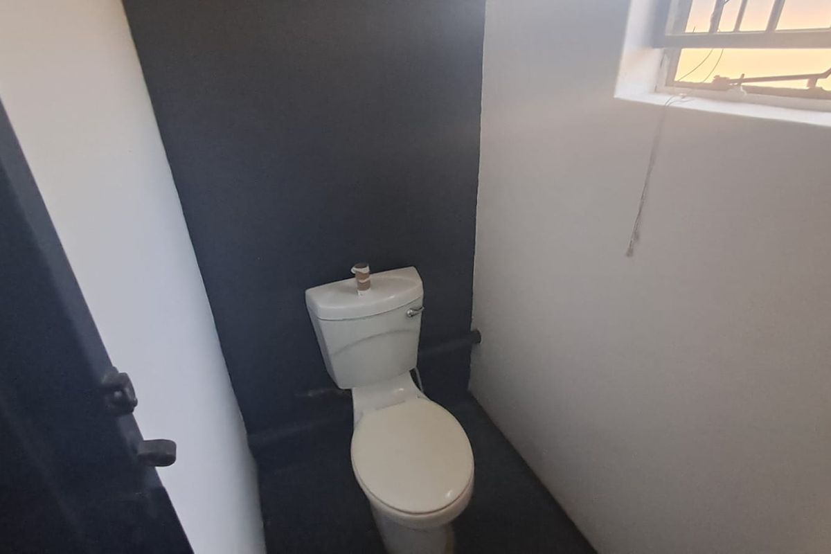 A small, functional bathroom featuring a toilet and a window with security bars, currently in need of minor repairs and cosmetic updates.