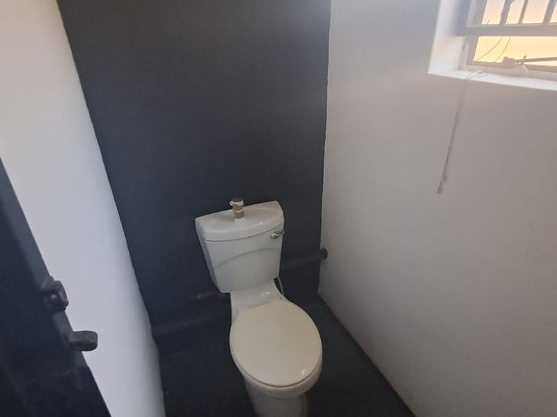 A small, functional bathroom featuring a toilet and a window with security bars, currently in need of minor repairs and cosmetic updates.