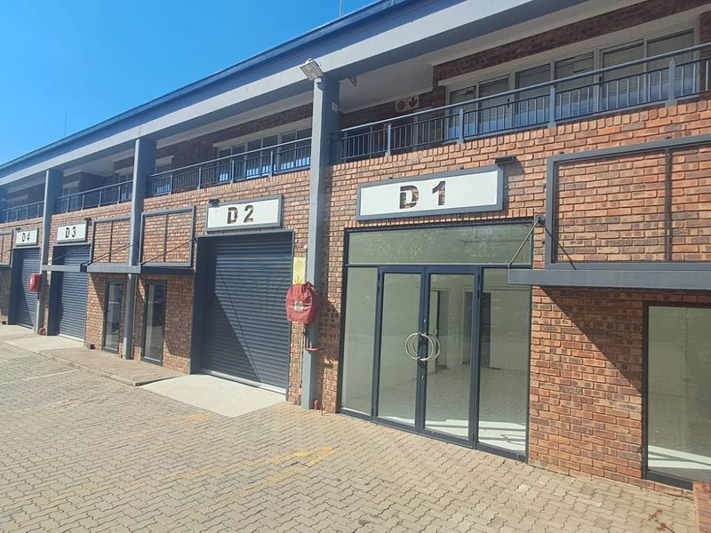 Front elevation of a multi-unit industrial complex featuring face brick construction, roller shutter doors, and glass storefront entrances with upper-level balcony access.