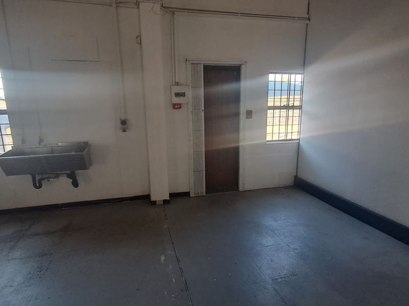 A functional industrial utility space featuring a wall-mounted sink, concrete flooring, and secure window bars, suitable for workshop or storage use.