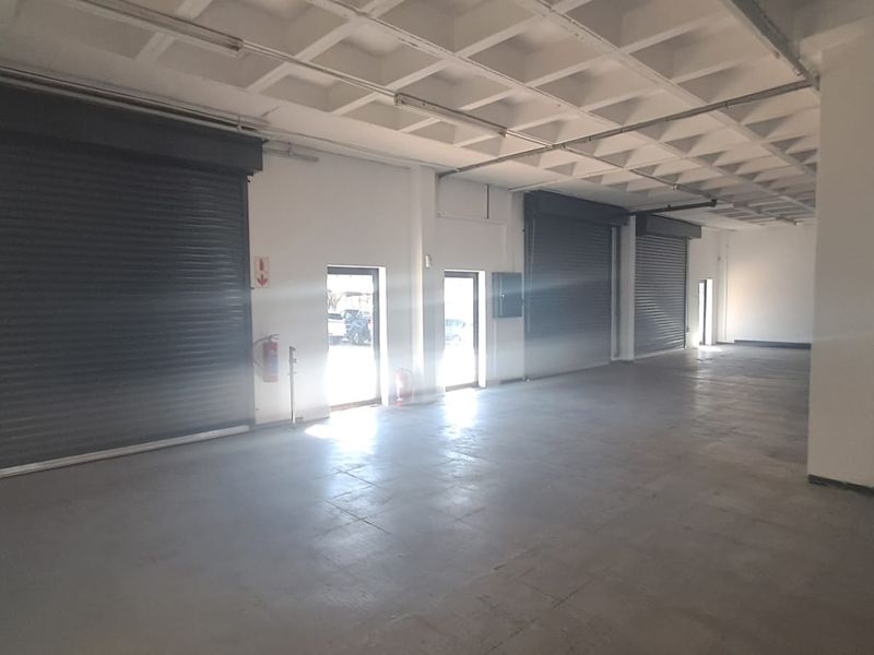 Spacious industrial warehouse or garage area featuring high-clearance waffle slab ceilings, concrete flooring, and multiple large roller shutter doors for easy access.