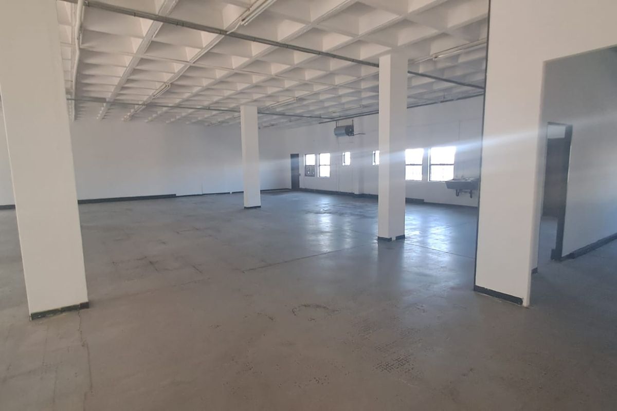 Spacious open-plan industrial unit featuring a waffle slab ceiling, concrete flooring, structural columns, and large windows providing ample natural light.