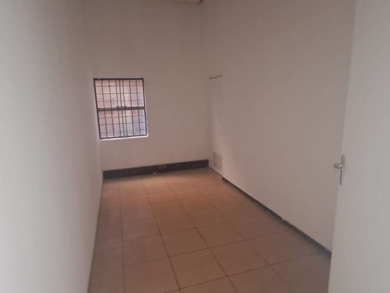 A vacant utility room featuring tiled flooring and a window with security bars, offering a blank canvas for various industrial or storage uses.