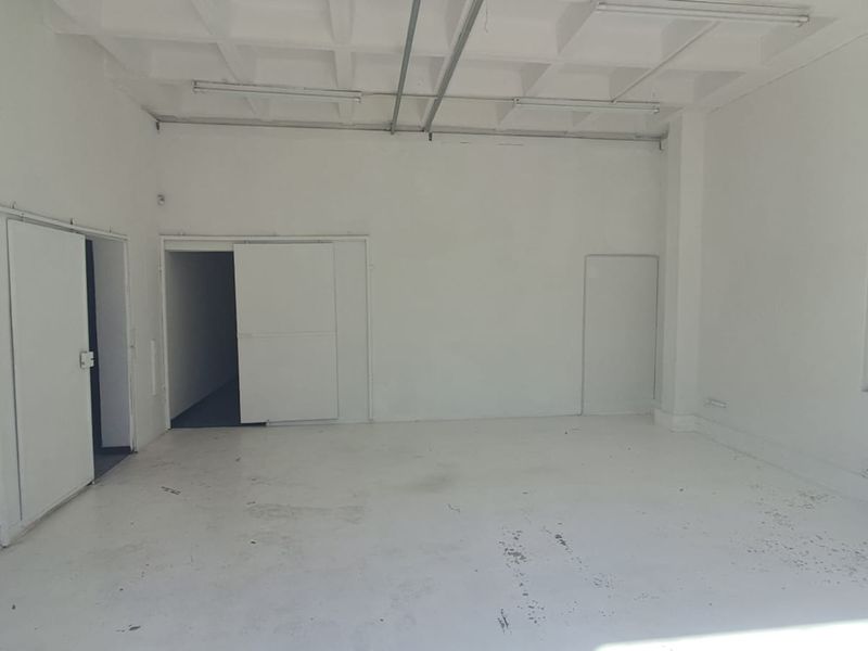 An empty industrial utility space featuring a waffle slab ceiling, exposed conduit, and secure window bars, suitable for storage or workshop use.