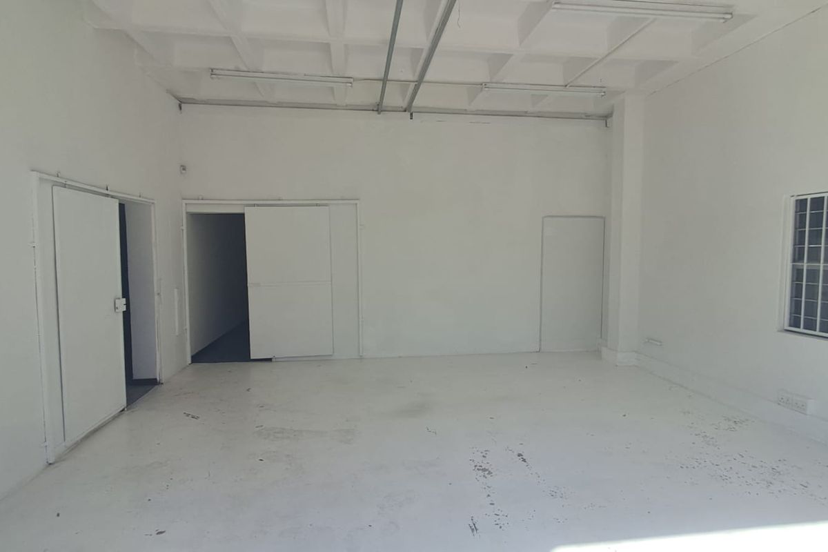 An empty industrial utility space featuring a waffle slab ceiling, exposed conduit, and secure window bars, suitable for storage or workshop use.