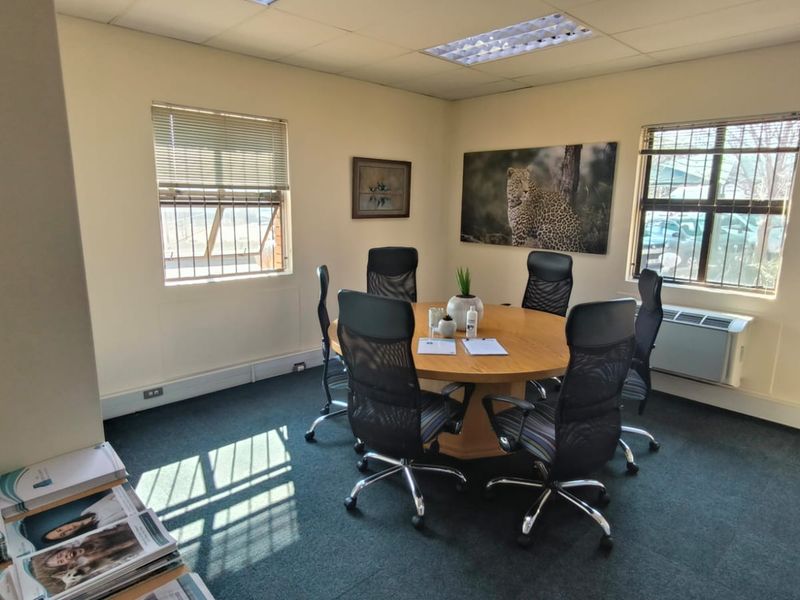 A functional office meeting room featuring carpeted floors, a suspended ceiling with recessed lighting, and a wall-mounted air conditioning unit.